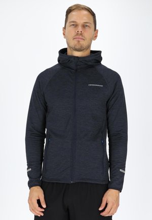 Navy zip-up hoodie made of textured fabric; features a fitted design, hood, and reflective accents on sleeves. Black athletic pants.