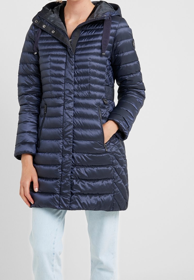 Laivastonsininen toppatakki pystysuuntaisella tikatulla kuviolla, vetoketjullisilla sivutaskuilla, säädettävällä hupulla ja nyöreillä sekä sileällä satiinimaisella pinnalla.