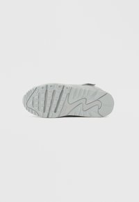 Világosszürke sportcipőtalp texturált gumiból, kiemelkedő, hullámos középtalp dizájnnal és mély tapadásnövelő hornyokkal a jobb fogás érdekében.