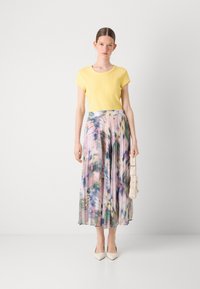 Haut jaune à manches courtes associé à une jupe maxi plissée colorée présentant des teintes pastel et des motifs abstraits. Complété par des talons crème.