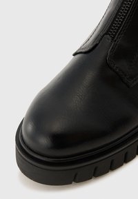 Bottine en cuir noir avec un bout arrondi, finition texturée, couture visible et semelle en caoutchouc épaisse avec des accents rainurés.