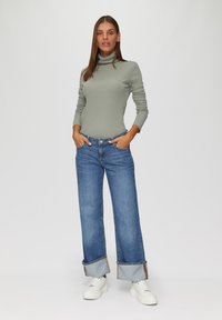 Jasnozielony golf, niebieskie szerokie dżinsy z podwiniętymi nogawkami i białe trampki. Tkanina jest gładka, a fason casualowy.