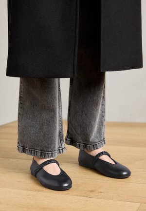 Czarne buty na niskim obcasie z zaokrąglonym noskiem i elastycznym paskiem na podbiciu, w zestawieniu z szerokimi, postrzępionymi szarymi dżinsami.