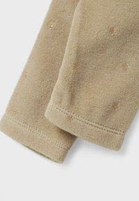 Tessuto in pile beige con una consistenza morbida, caratterizzato da piccoli dettagli dorati disposti in un motivo sparso sulla superficie. Margini lavorati a maglia visibili.