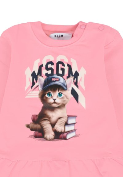 Chemise rose avec un chaton portant une casquette noire étiquetée MSGM, assis sur des livres empilés avec le texte MSGM en arrière-plan.