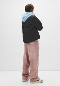 Dynejakke i sort med en lyseblå hætte, parret med løse pink jeans. Sneakers med grønne accenter fuldender looket.