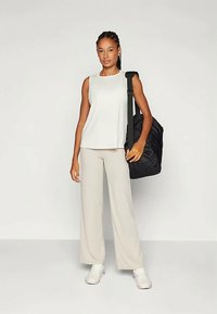 Světlé šedé bezramínkové tričko, béžové široké kalhoty a bílé tenisky. Černá volná taška zavěšená přes rameno. Hladká tkanina a uvolněný střih.