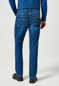 Vaqueros de mezclilla azul con un diseño de pierna recta, que cuentan con dos bolsillos traseros con costura en forma de flecha y una etiqueta de cuero en la cinturilla.