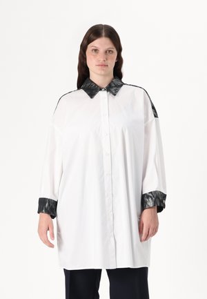 White shirt with a black, textured collar and cuffs. Features a button front and loose fit with long sleeves. Smooth fabric, minimal design.