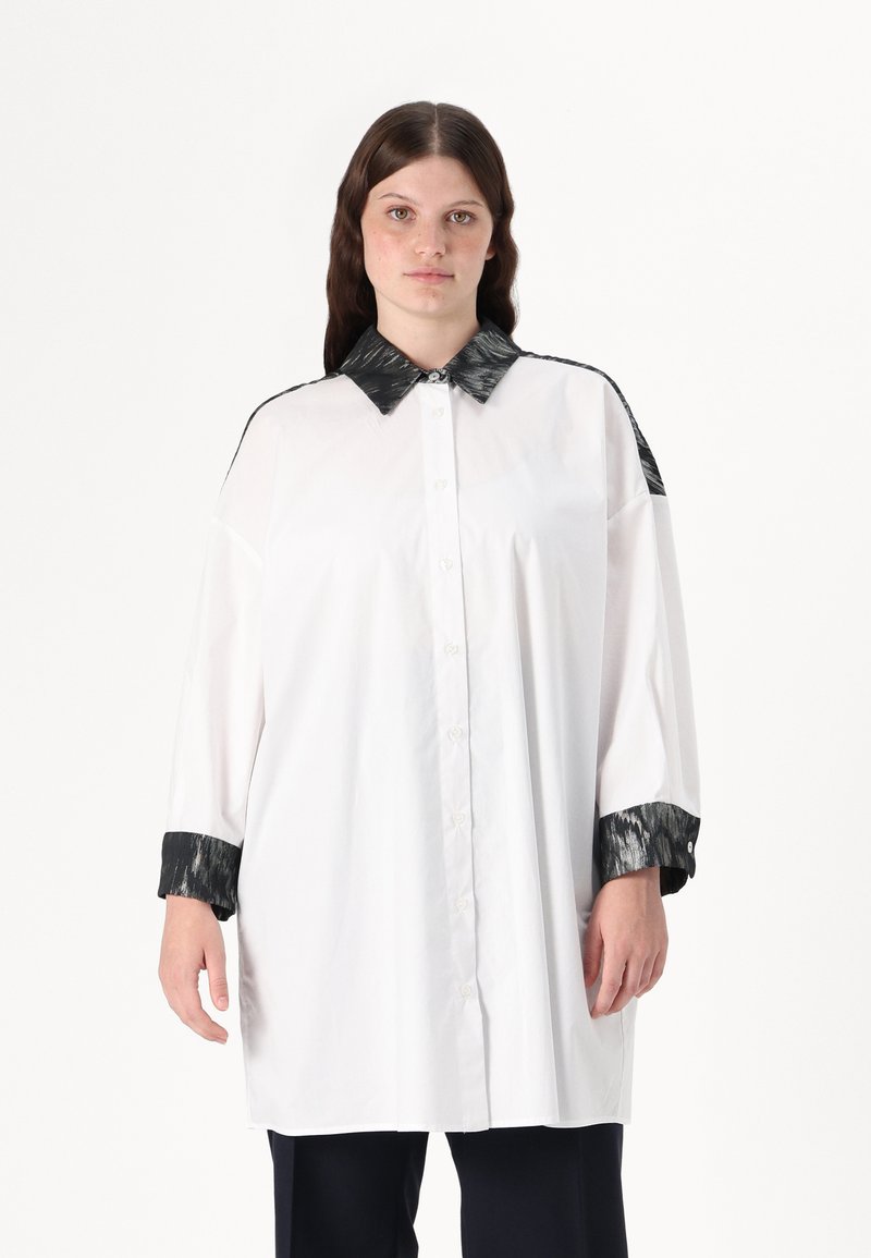 Hvit skjorte med en svart, teksturert krage og mansjetter. Har knapper foran og løs passform med lange ermer. Glatt stoff, minimalistisk design.