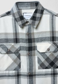 Camicia con bottoni a quadri larghi in bianco, grigio e nero, due tasche sul petto con bottoni e colletto a punta.