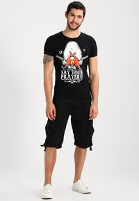 Black t-shirt with a cartoon graphic and text reading "SAY YOUR PRAYERS!" paired with black cargo shorts and white sneakers.