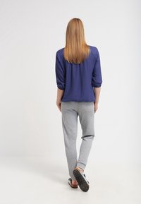 Marinblus, lätt topp med trekvartslånga ärmar, kombinerad med grå, strukturerade, smalnande joggbyxor och svarta slip-on skor.