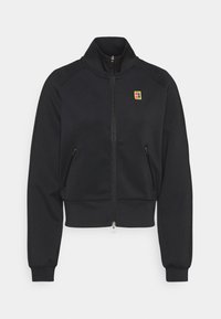 Chaqueta negra con cremallera, confeccionada en una tela suave, con mangas raglán, dos bolsillos con cremallera y un pequeño logo colorido en el pecho.