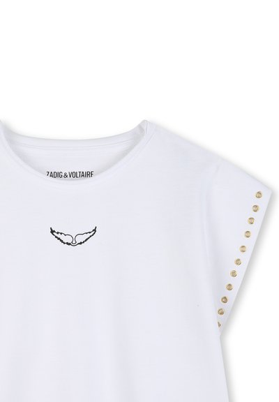 T-shirt blanc à col rond avec logo de cœur ailé noir sous le col et œillets dorés alignés verticalement sur la manche droite.