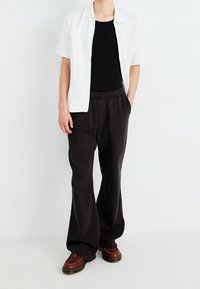 Chemise blanche à manches courtes, débardeur noir, pantalon noir ample et chaussures marron avec semelle texturée. Design simple et moderne.