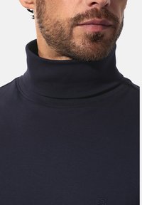 Marineblauer Rollkragenpullover aus weichem Material, mit einem enganliegenden Kragen und glatter Textur. Dezentes Logo-Detail am Saum.