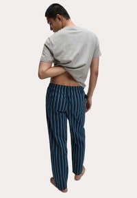 Šedé tričko s krátkým rukávem a modré pyžamové kalhoty s proužky. Kalhoty mají vertikální proužky v různých odstínech modré. Jednoduchý, pohodlný střih.