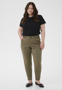 Olijfgroene op maat gemaakte broek met een normale taille, vlakke voorkant, zijzakken en een knoopsluiting. Gecombineerd met een zwart T-shirt met korte mouwen.