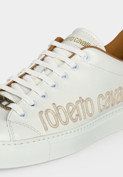 Baskets en cuir blanc avec lacets blancs et broderie beige "roberto cavalli" sur le côté, et logo doré sur la languette.