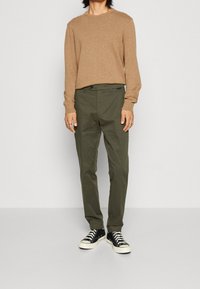 Brun stickad tröja, olivgröna byxor, svartvita sneakers. Outfiten har en avslappnad passform med långa ärmar och inga synliga mönster.