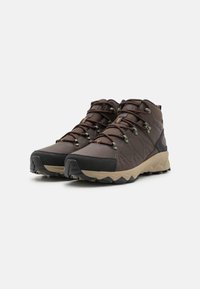 Botas de senderismo marrones con un upper texturizado, paneles de malla y una puntera de goma negra. Presentan una suela de color claro en contraste y ojales de metal.