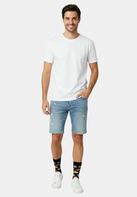 Camiseta blanca de cuello redondo, shorts de mezclilla azul claro con detalles desgastados, calcetines negros con motivos de sushi y zapatillas blancas.