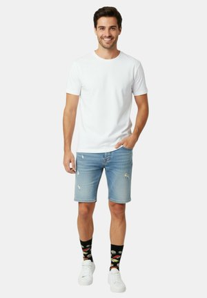 Hvid T-shirt med rund hals, lyseblå denimshorts med slidte detaljer, sorte sokker med sushimønster og hvide sneakers.