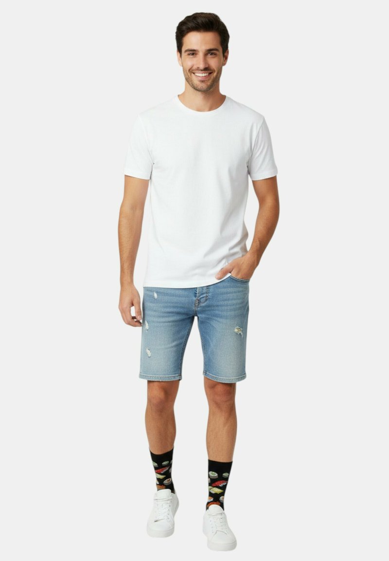 Camiseta blanca de cuello redondo, shorts de mezclilla azul claro con detalles desgastados, calcetines negros con motivos de sushi y zapatillas blancas.