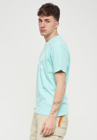 T-shirt di cotone azzurro chiaro con maniche corte, caratterizzato da testo stampato bianco. Indossato con pantaloni cargo beige. Collo rotondo semplice.