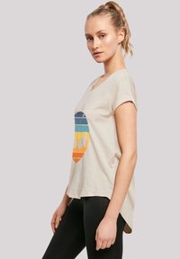 Cotton t-shirt in light beige, featuring a multicolored, retro-style graphic of stripes and an emblem. Short sleeves, rounded neckline, relaxed fit.