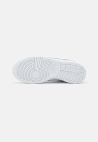 Semelle de sneaker blanche avec un motif circulaire et une texture antidérapante. Une marque notable est visible dans la zone du talon. Design épuré sans ornements.
