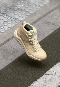 Helle beige Wanderschuhe mit strukturierter Oberfläche, Schnürdesign, verstärktem Absatz und Gummisohle. Verfügt über Polsterung und Griffdetails.