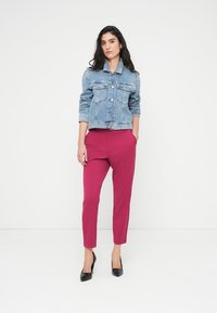 Τζιν σακάκι με ανοιχτό μπλε πλύσιμο, με μπροστινές τσέπες. Ροζ παντελόνια εφαρμοστά, με ψηλόμεσο και στενή γραμμή, και κομψά μαύρα ψηλοτάκουνα.