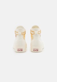 Vita höga sneakers i canvas med guldkedjedetaljer och en röd logotyp. Platta gummisulor, sydda detaljer och en texturerad ovandel.