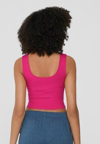 Top corto aderente in tessuto ribbed di un vivace rosa, con scollatura rotonda e spalline spesse. Abbinato a pantaloni larghi e texturizzati di colore blu.