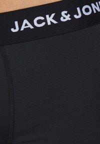 Schwarze Boxershorts aus glattem Material, mit einem breiten schwarzen elastischen Bund, auf dem "JACK & JONES" in weißer Schrift steht.