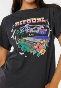 Camiseta de algodón negra con un diseño gráfico colorido de una escena de carretera que incluye elementos tropicales, flores y el texto "Ripcurl Route 99."