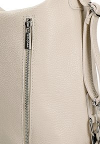 Beige leren handtas met een gestructureerd oppervlak, een zilveren ritssluiting en een afneembare schouderriem met metalen accenten.
