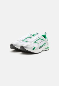 Hvite sneakers med grønne detaljer, mesh overdel, polstret krage, rund tå, svart gummisåle og et karakteristisk logo på siden.