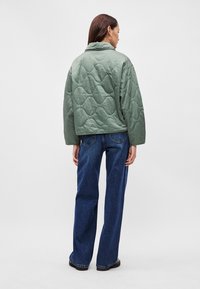 Κουβερτίνα πράσινη τζάκετ με γιακά, με κουτί σχήμα και υφή στην επιφάνεια. Συνδυάζεται με φαρδιά, σκούρα μπλε τζιν και μαύρα υποδήματα.