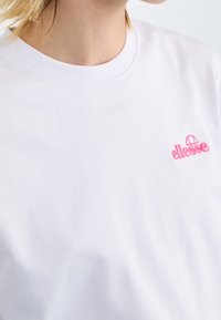 Witte katoenen t-shirt met een ronde hals en korte mouwen, voorzien van een klein, roze geborduurd logo op de borst. Stijlvolle textuur.