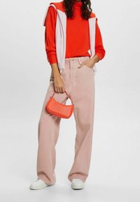 Roter gestrickter Pullover, rosa weite Hose und eine hellrosa Weste. Die Accessoires umfassen eine kleine orangefarbene Handtasche und weiße Sneakers.