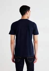 Marineblå bomull T-skjorte med kortermede, klassisk rund hals, glatt tekstur og uten synlige grafikker. Brukt med mørke jeans.