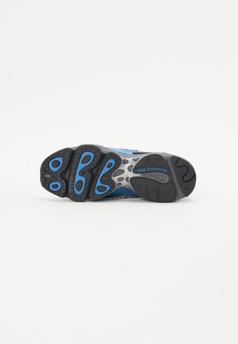 New Balance Sneaker mit einer schwarzen Gummisohle, blauen Akzenten, silbernen Details und einem strukturierten Oberdesign.
