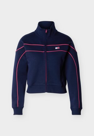 Veste zippée bleu marine avec col montant, passepoil rose sur les manches et la poitrine, et un petit logo rectangulaire sur le côté gauche de la poitrine.