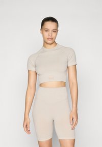 Bež prugasti cropped top s kratkim rukavima u kombinaciji s hlačama visokog struka. Glatka tekstura, minimalno brendiranje i uski dizajn.