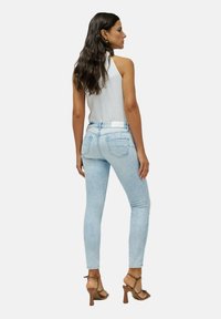 Jeans skinny de denim en un azul claro, con una cintura media, bolsillos traseros y una etiqueta blanca de la marca en la cintura. Modelo combinado con tacones marrones.