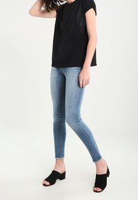 Mustapaitainen lyhythihainen t-paita, jossa on pitsikuosi, yhdistettynä vaaleansinisiin tiukkoihin farkkuihin ja mustiin avonaisiin heel-mule-korkokenkiin.