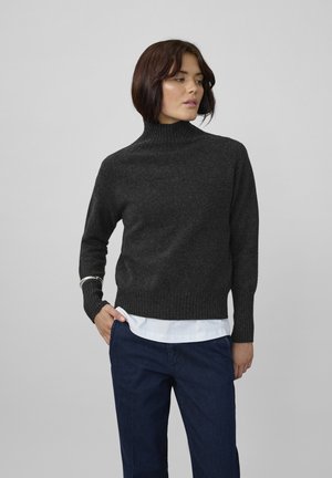 Temno siva, rebrasta turtleneck pulover iz teksturiranega pletenega materiala, v družbi bele srajce, nosi se z mornarsko modrimi hlačami.